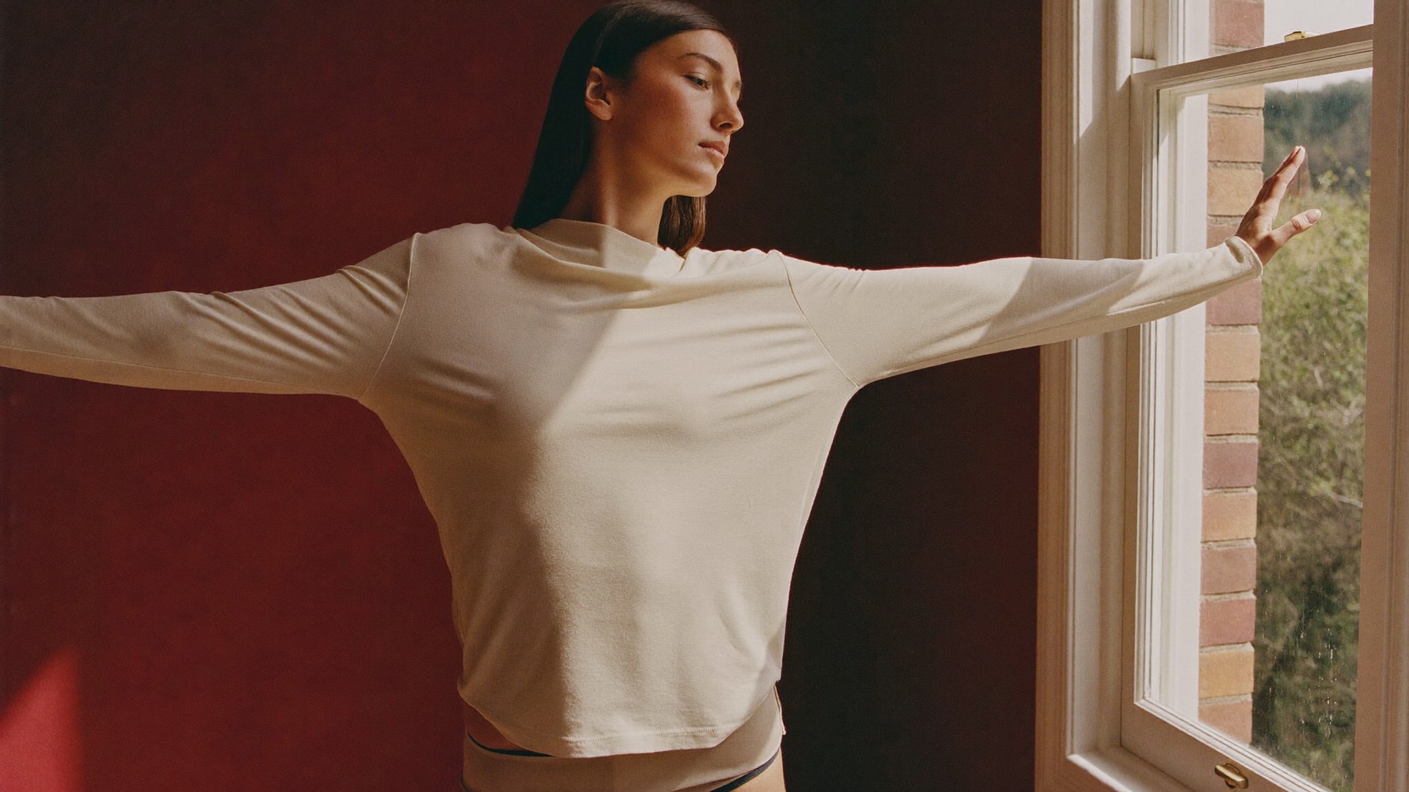 A woman standing tall and at ease by a window, relieved of a weight she carried for years